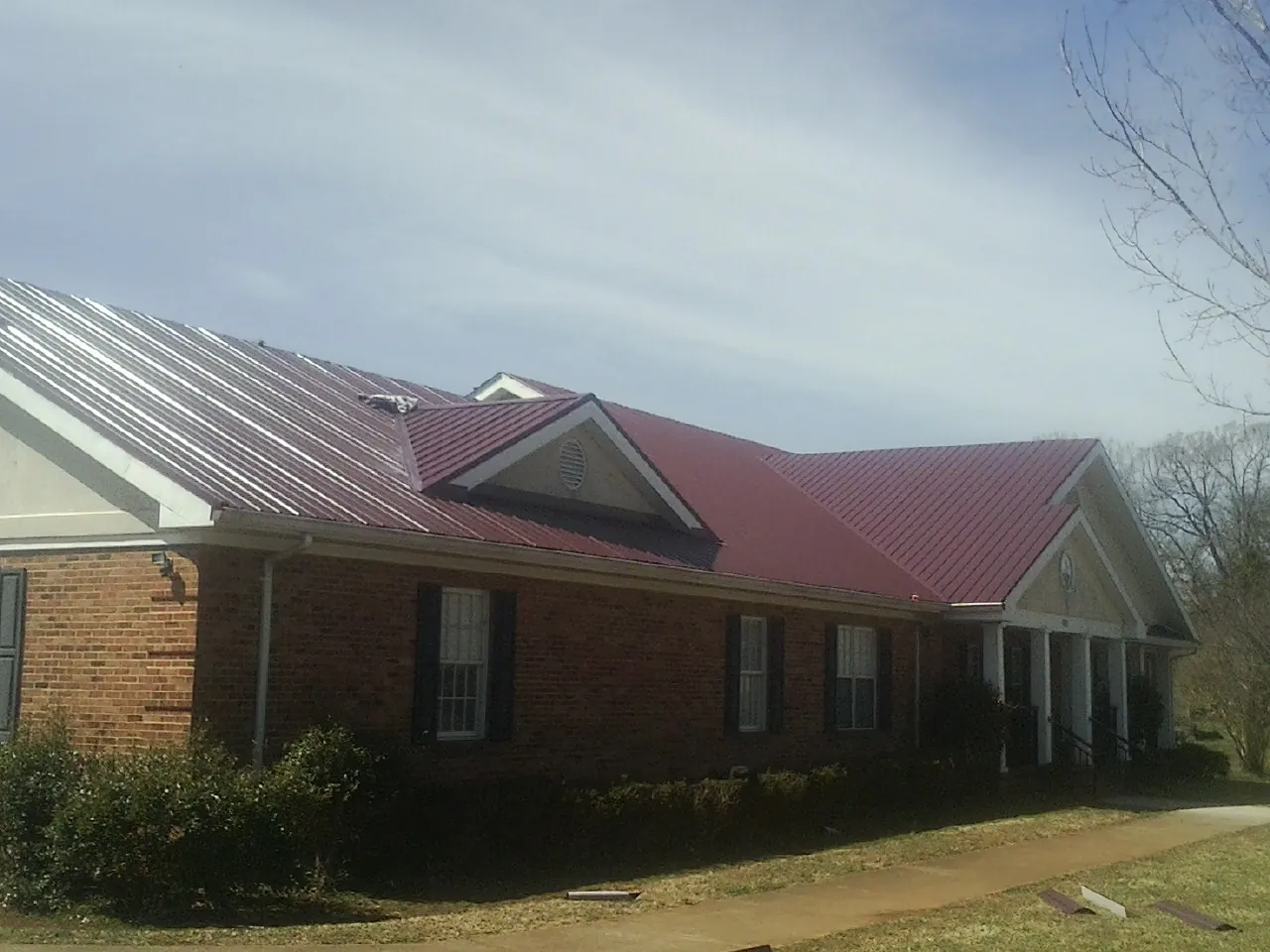Red metal roof with gabled entries on a long brick building, from a Hail Damage Roof Repair job in Daisytown