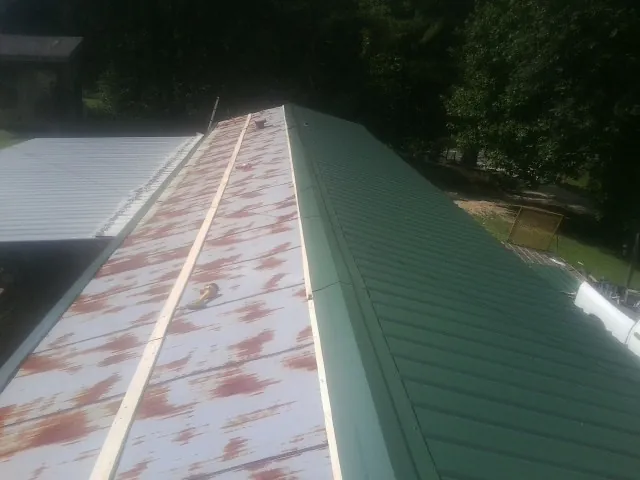 Old rusted panels beside newly installed green metal roofing — Wind Damage Roof Repair by Roofing Brothers in Daisytown