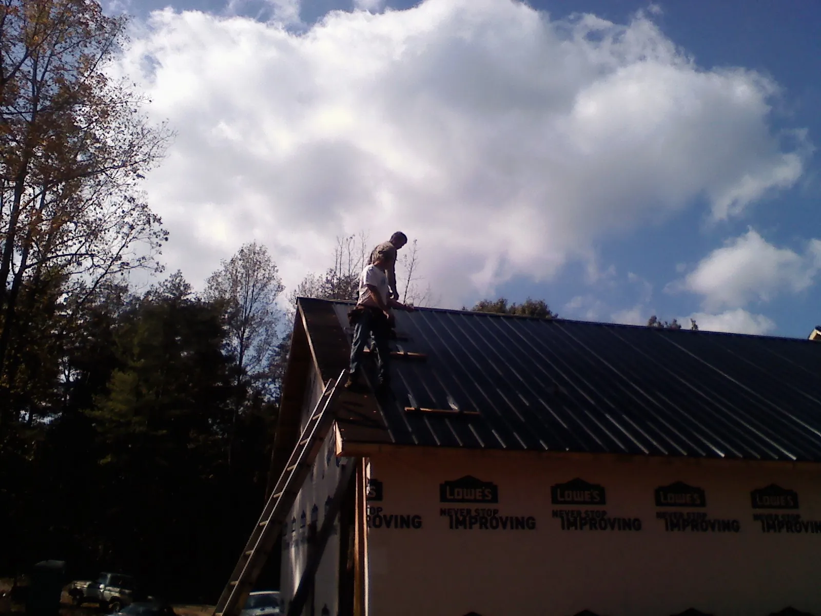Roofer fastening dark metal panels high against a cloudy sky, from a Roof Inspection job in Daisytown