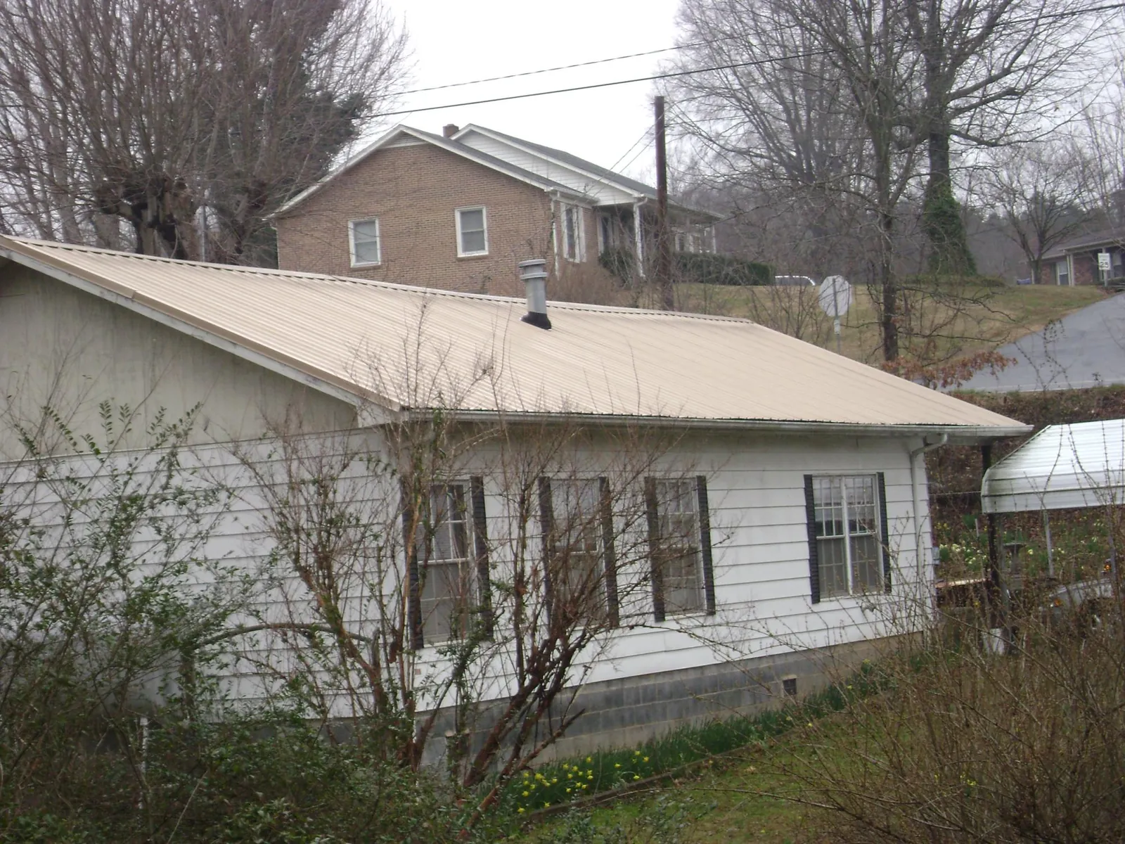 Tan metal roof on a white sided house set into a hillside — Commercial Roofing by Roofing Brothers in Daisytown